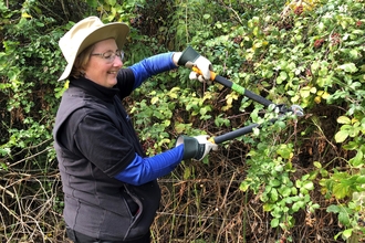 Woman using a pair of loppers on a bramble hedge by Katie McEvoy