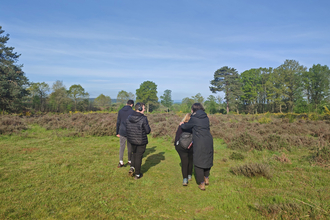 Four people walking away from the photographer in a heathland environment with a blue sky above them by Beccy Somers