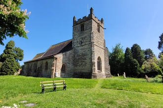 Friends of Feckenham Church surrounded by its grounds. There is a bench visible to the left.