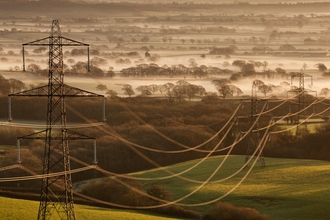 Electricity pylons and cables stretching across a landscape by Guy Edwardes/2020VISION