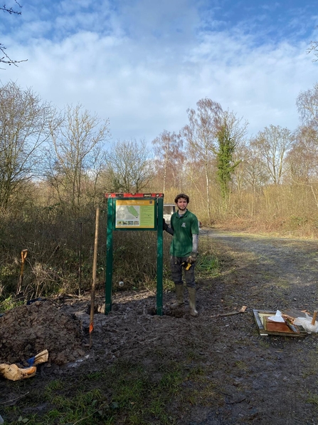 Jake standing by a newly installed interpretation sign alongside a woodland ride 