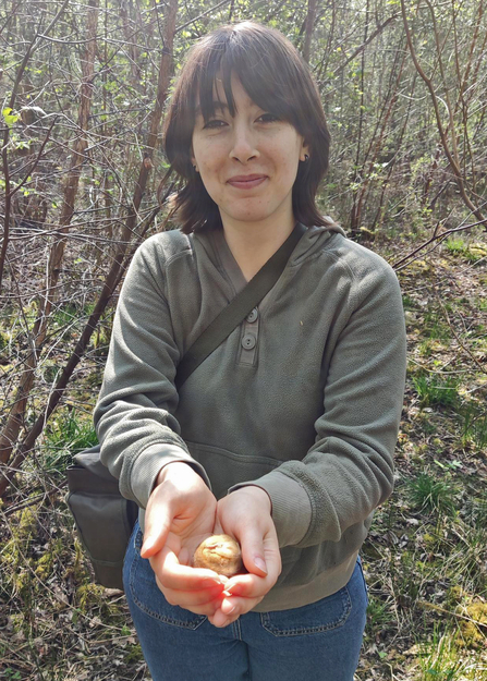 Woman with dark hair, smiling and looking at the camera as she holds a dormouse in the palm of her hands
