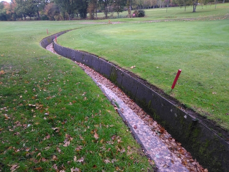 A concrete slab lined ditch running through a golf course