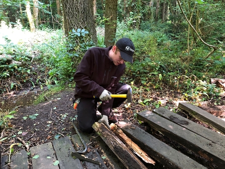 Man taking apart a boardwalk through a woodland