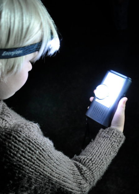 Young person holding a bat detector with a head torch pointing at the detector by Emma Bradshaw