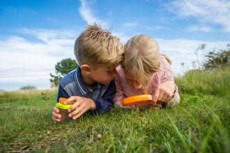 Two children looking for bugs in a meadow by Matthew Roberts