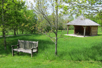 Park bench and shelter in grassland with trees