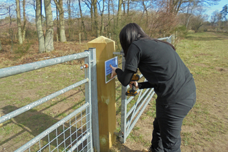 Woman dressed in black securing a sign onto a gate post