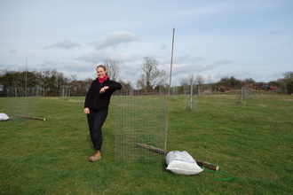 Issy leaning on the tree guard of a fruit tree that she's recently planted as part of new orchard planting