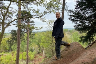 Woman standing on top of The Devil's Spittleful sandstone rock overlooking trees