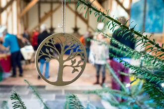 Decoration hanging from tree with people shopping in the area behind it by Ruth Bourne