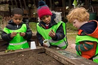 Three children looking at something they've found in the soil by Penny Dixie