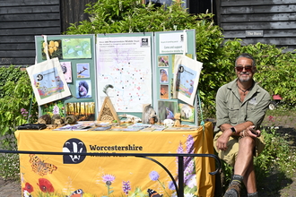Man sitting next to a Worcestershire Wildlife Trust branded stall in the sunshine (by Brian Taylor)