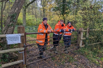 Conservation trainees and Andy leaning on a gate in a woodland