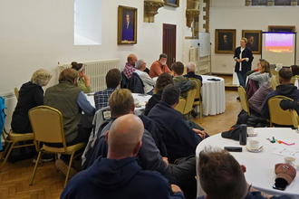 Group of people in a building, person at the front listening to a group member and group sitting at different tables