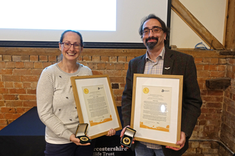 Becky Lashley and Cody Levine holding their framed certificates and medals; both are smiling at the camera
