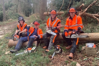 Trainees sat on a fallen tree with chainsaws