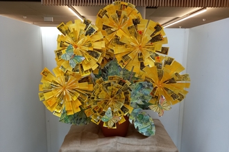 An art installation made of very large paper dandelion flowers. It's in a building and is surrounded by three white low 'walls'