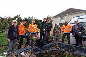 8 people standing around a newly restored pond, smiling at the camera after a day's hard work