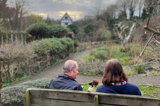 A photograph of a podcast host interviewing a staff member sitting on a bench in a garden