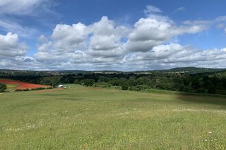 It's a lovely sunny day with white fluffy clouds in the sky. The photographer is at a high point in a landscape looking out across green fields to the heathland of The Devil's Spittleful in the distance