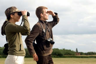 Two people looking through binoculars by Zsuzsanna Bird