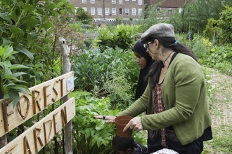 Two people standing in front of a 'forest garden' sign looking into the vegetation; housing is the background