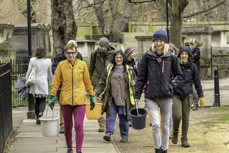 A group of smiling people carrying buckets and walking down a street