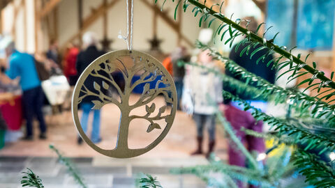 Decoration hanging from tree with people shopping in the area behind it by Ruth Bourne