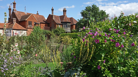A flower-filled garden with a red brick house in the background