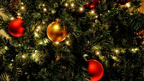 Red and gold baubles hanging on a christmas tree that's covered in fairy lights