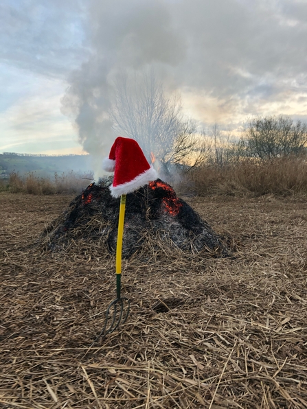 Santa hat hung up on fork in front of bonfire by Ruthie Cooper