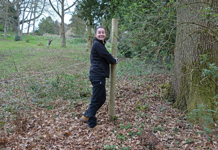 Woman installing a fence post and smiling at the camera by Ruthie Cooper