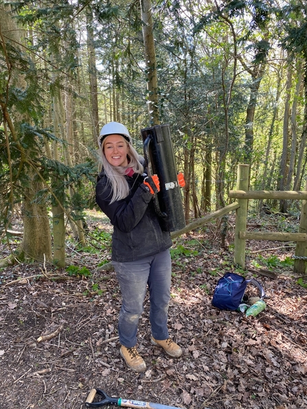 Young woman holding a fence post rammer in a woodland