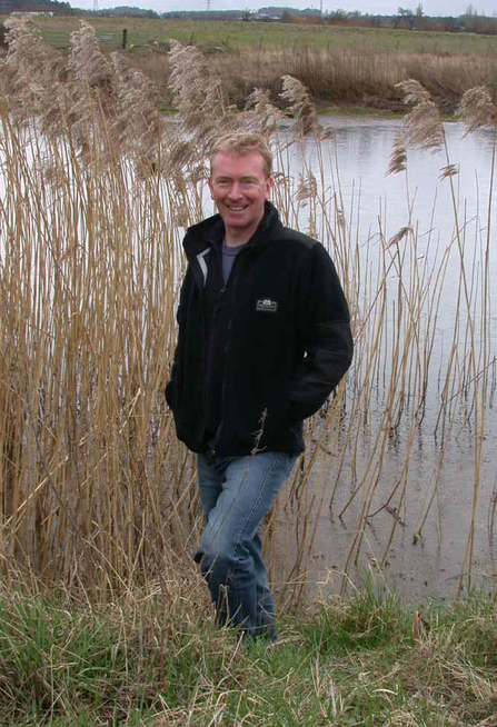 Andy Graham standing in front of reeds with water behind