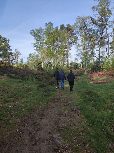 three people walking along a path at The Devil's Spittleful with trees in the distance and a blue sky by Beccy Somers