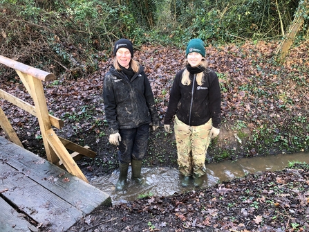 Two women standing in a ditch and grinning at the camera