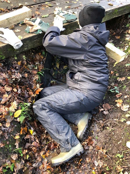 Person in waterproof clothing and hat sitting on the floor underneath a low bridge