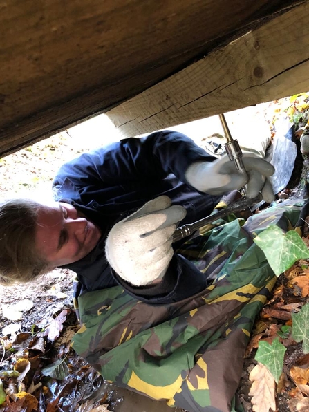 A woman lying on the floor under a bridge, smiling as she fits bolts to the underneath of the bridge