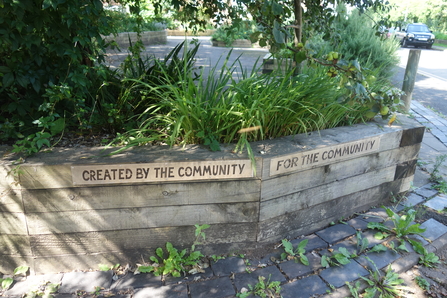 Raised bed in a community greenspace with the words "created by the community for the community" carved into it by Liz Yorke