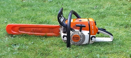 An orange chainsaw lay sideways on lawn