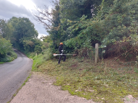 Matt stood with a brush-cutter with a road to the left