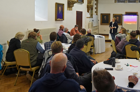 Group of people in a building, person at the front listening to a group member and group sitting at different tables