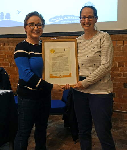 Two women holding a framed certificate between them and smiling at the camera