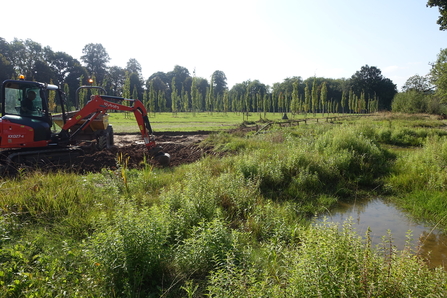 A digger is creating a new wetland near an existing pond