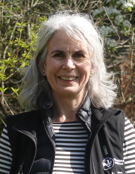 Woman with shoulder-length white/grey hair smiling at the camera on a sunny day
