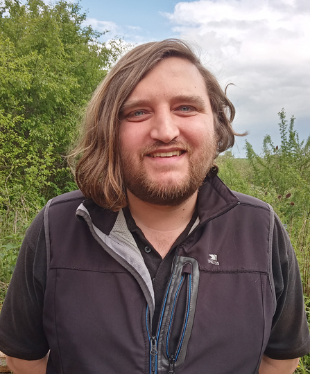 Person with a beard and long hair on one side smiling at the camera