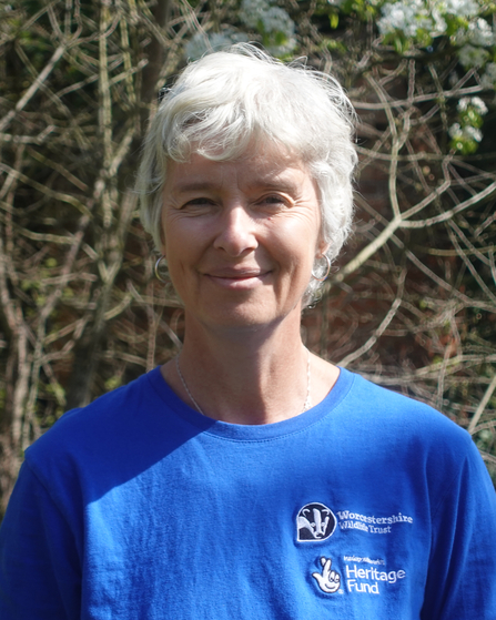 Woman with short white hair looking at the camera, wearing a blue top with the logos of Worcestershire Wildlife Trust and The National Lottery Heritage Fund