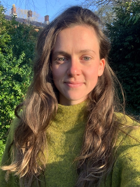 Woman with long brown hair smiling at the camera on a sunny day