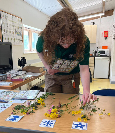 A person with long, curly hair sorting through a range of flowers on a table